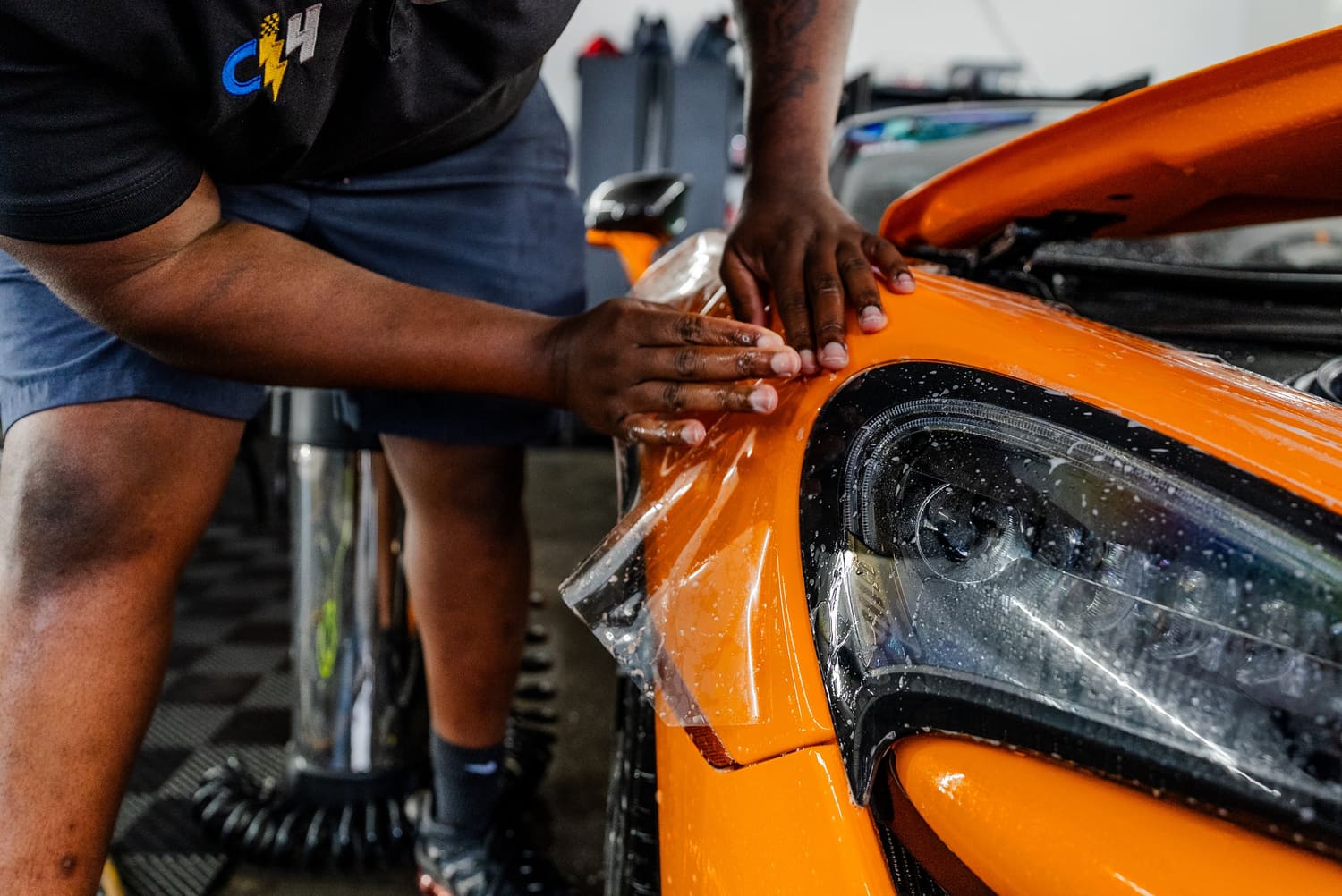 Installer smoothing paint protection film over the headlight of an orange sports car