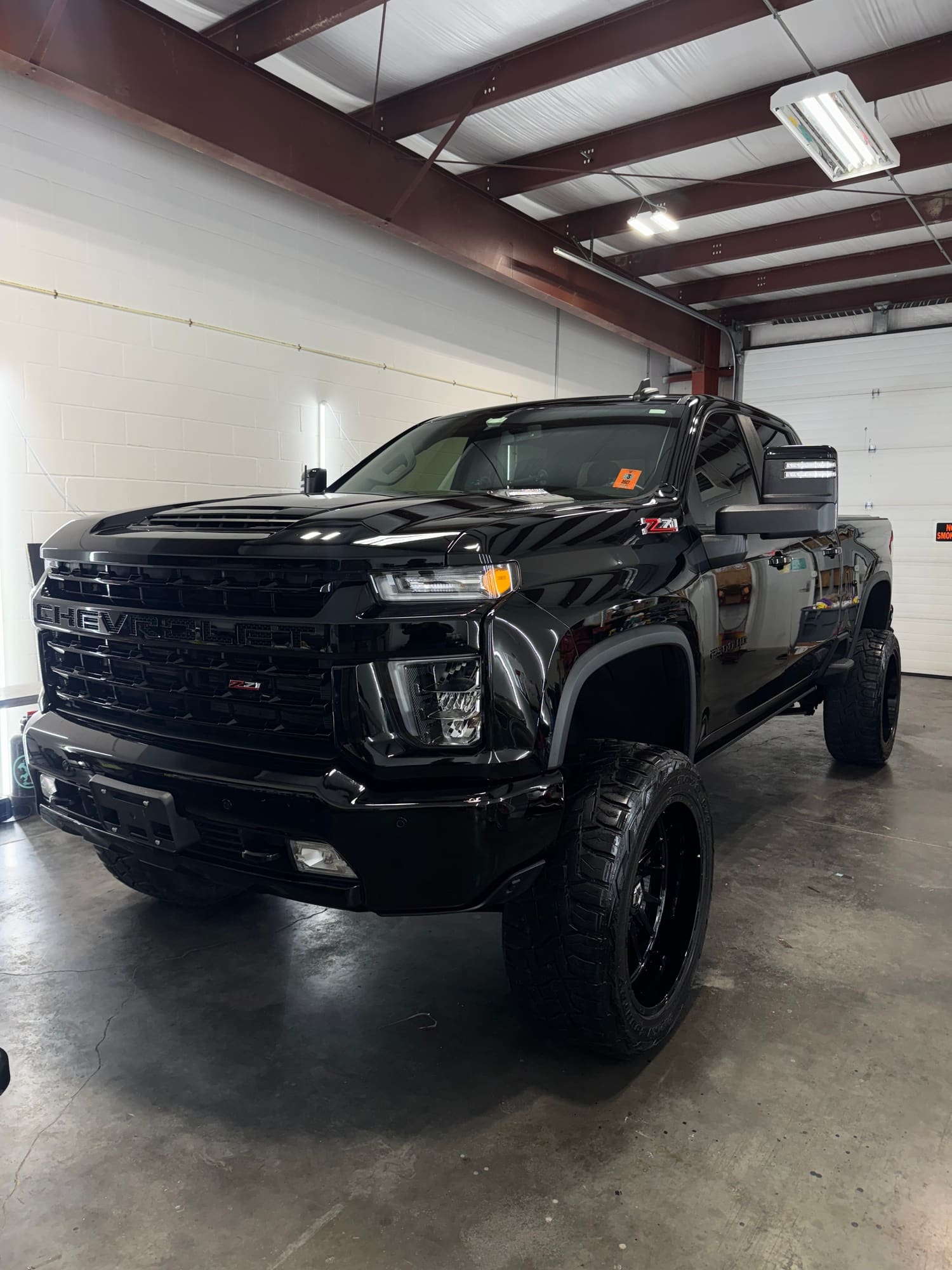 A black Chevrolet pickup truck with large off-road tires inside a garage or warehouse.
