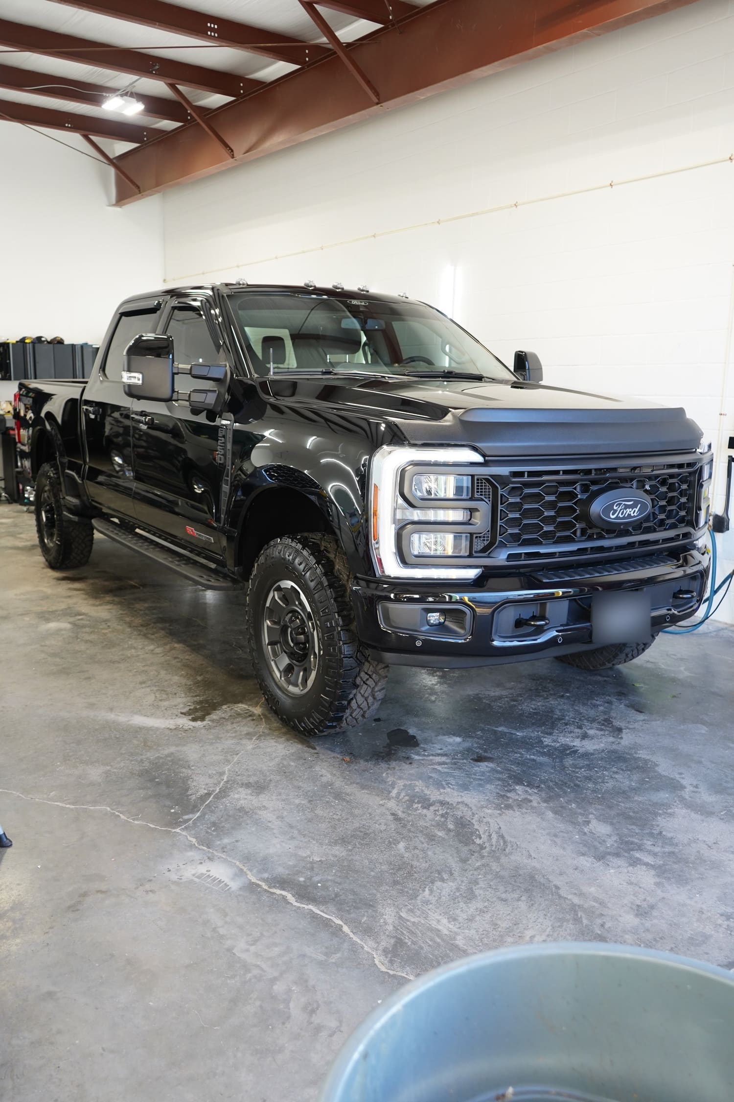 Black Ford pickup truck parked indoors on wet concrete floor in a garage or service area.