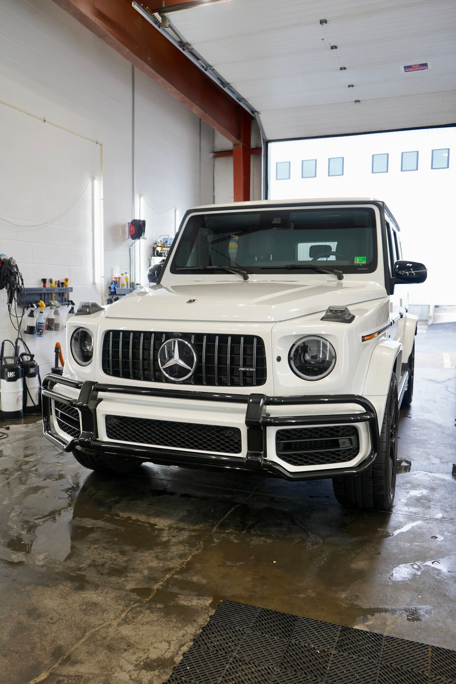 White Mercedes-Benz G-Class SUV inside a garage with tools on the wall and wet floor.
