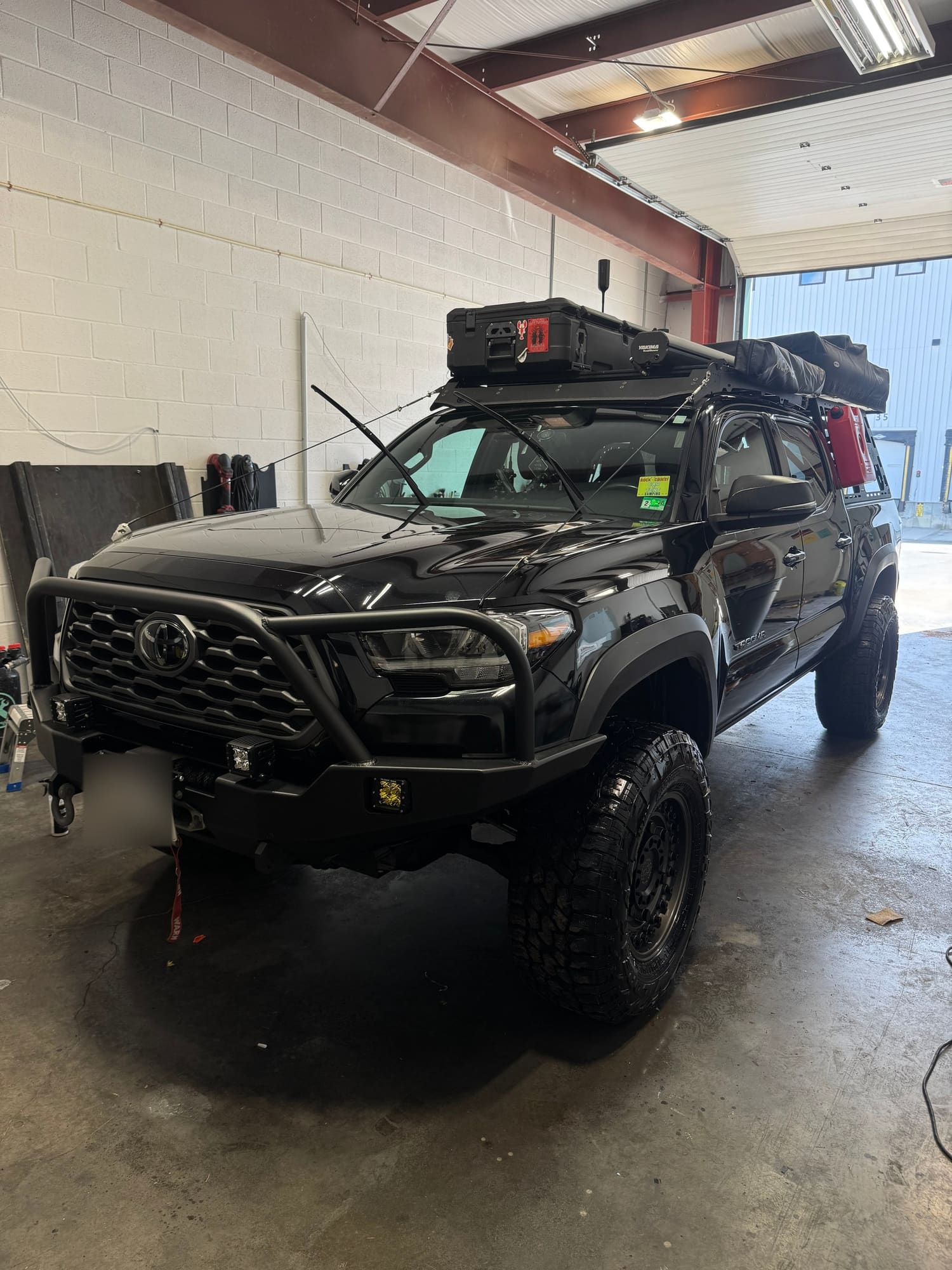Black Toyota off-road vehicle with front bumper guard, roof cargo rack with gear, mounted on a concrete floor in a garage or warehouse.