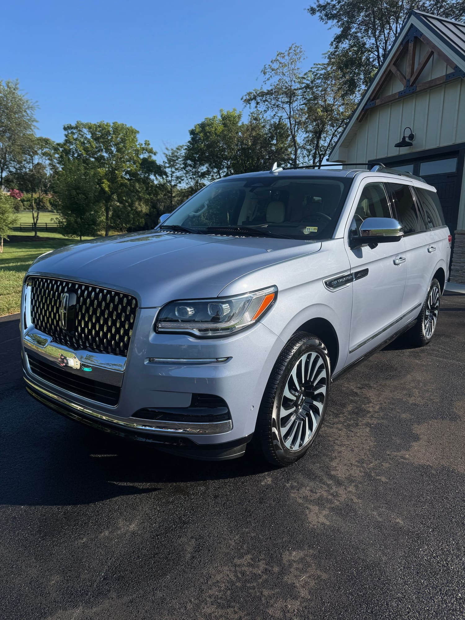 A silver Lincoln Navigator SUV parked on a driveway with a house and trees in the background on a sunny day.