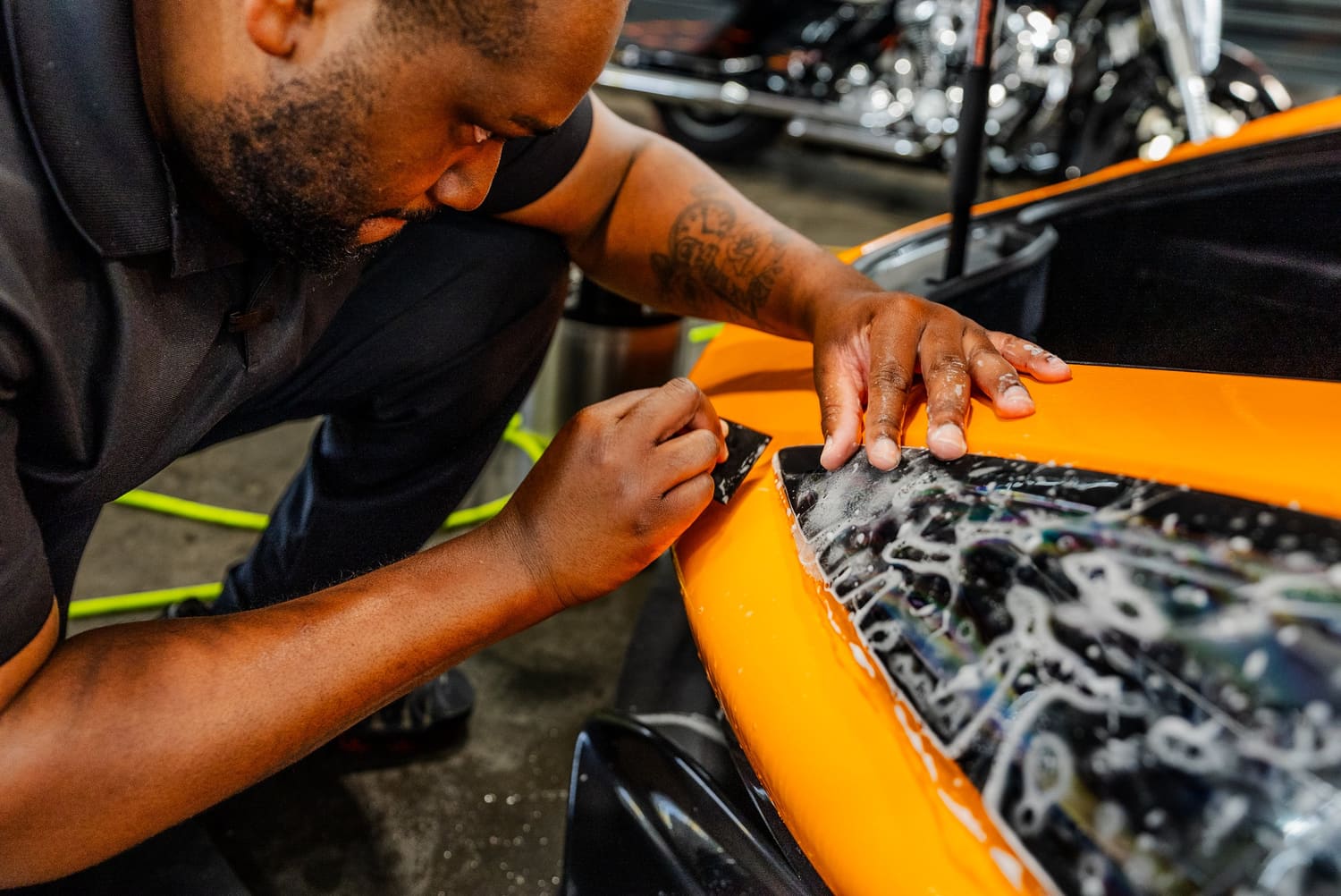 Installer applying paint protection film to the front of an orange sports car