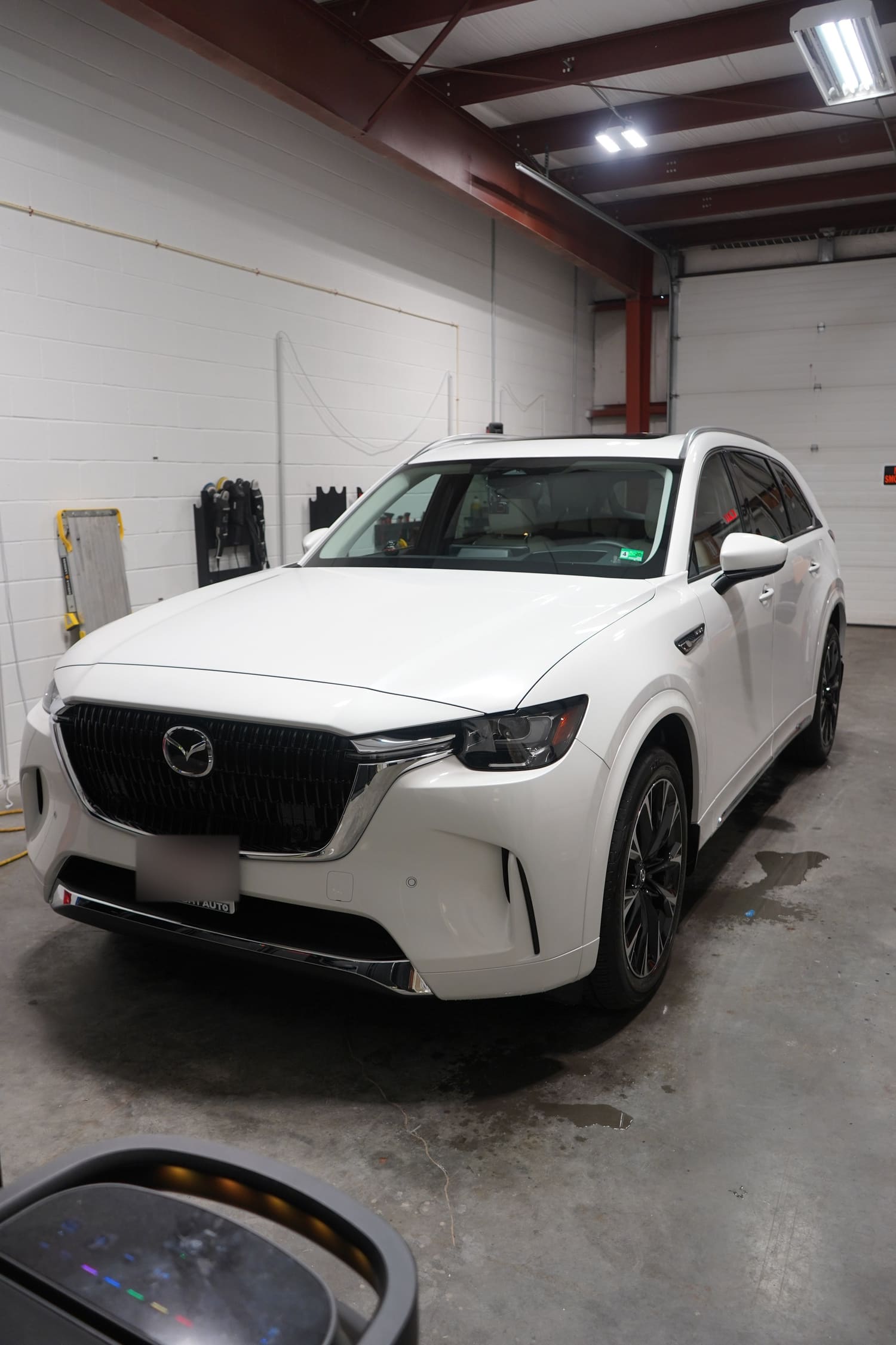 A white Mazda SUV parked inside a garage or service area with a white brick wall and closed garage door in the background.
