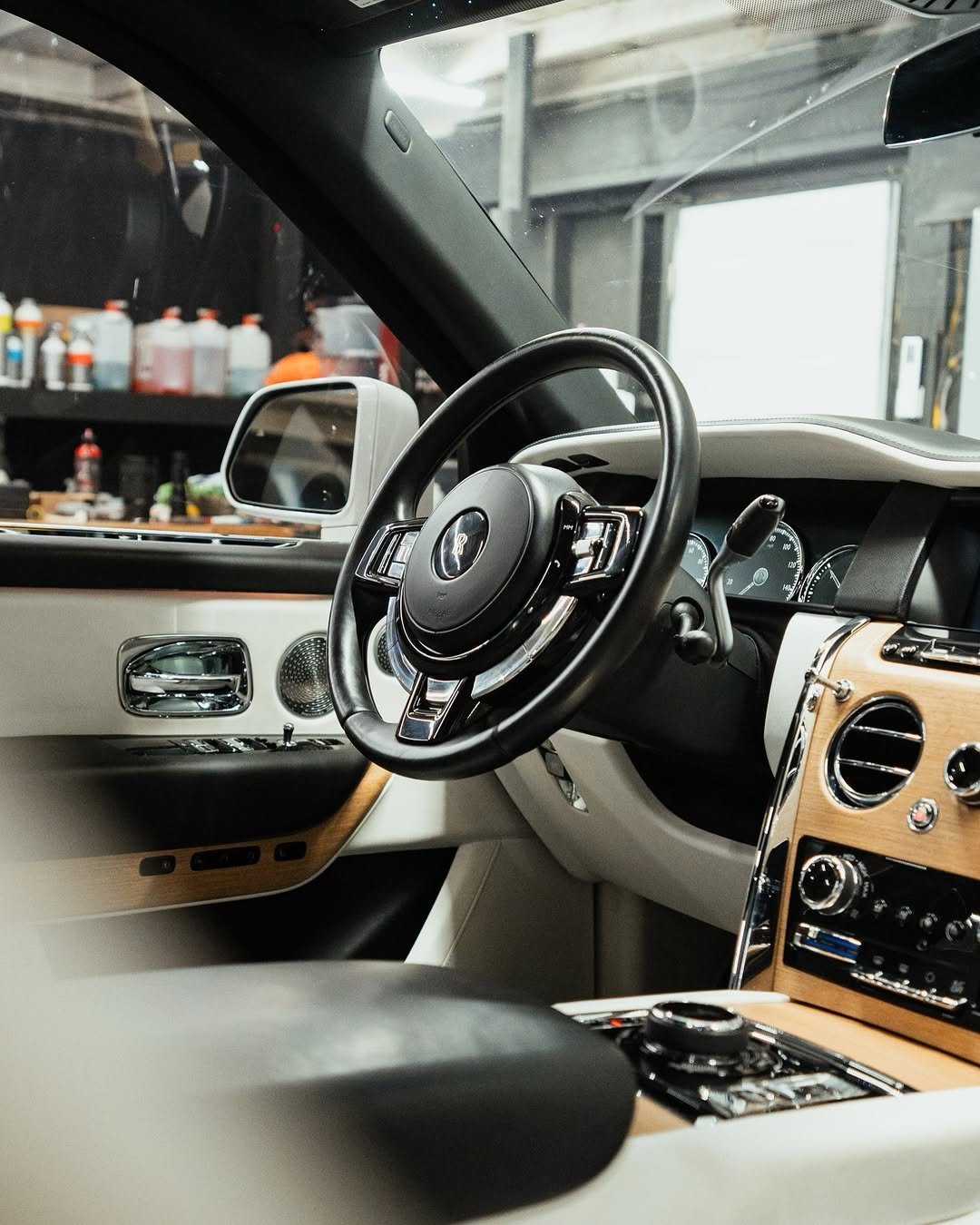 Interior of a luxury car showing a black steering wheel, dashboard with gauges, and a wood-trimmed center console.
