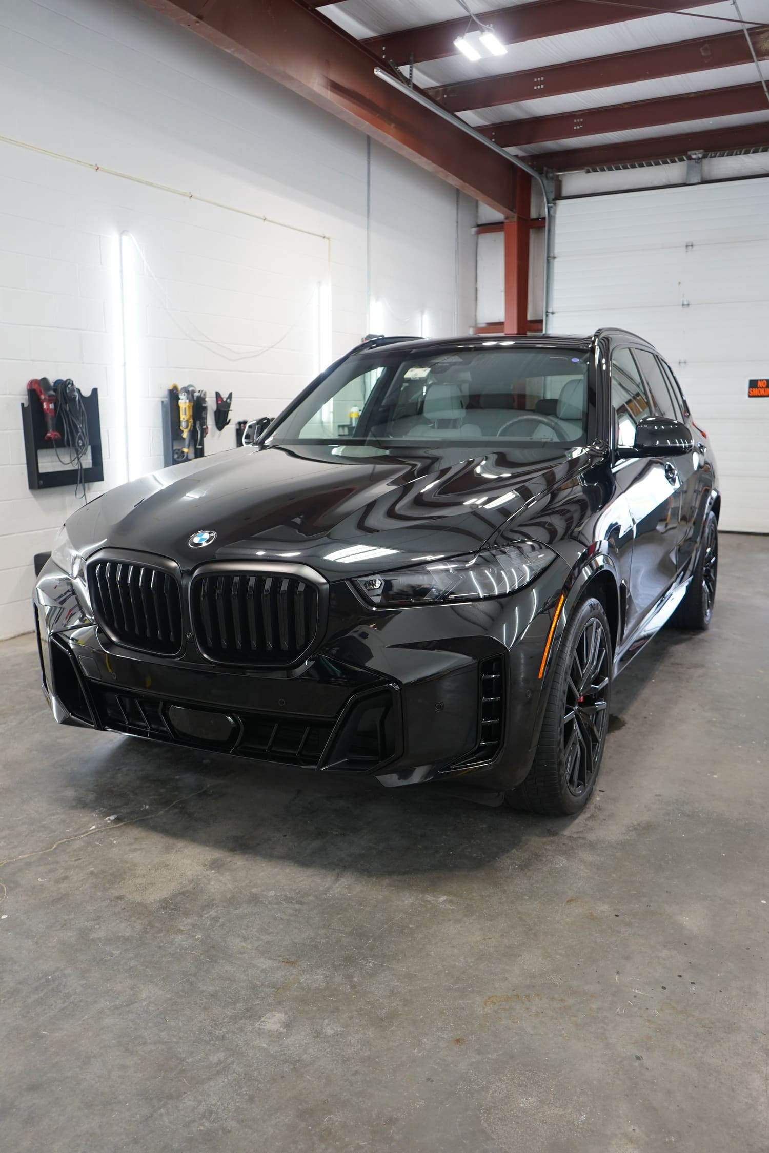 A black BMW SUV parked inside an industrial garage with tools on the wall.