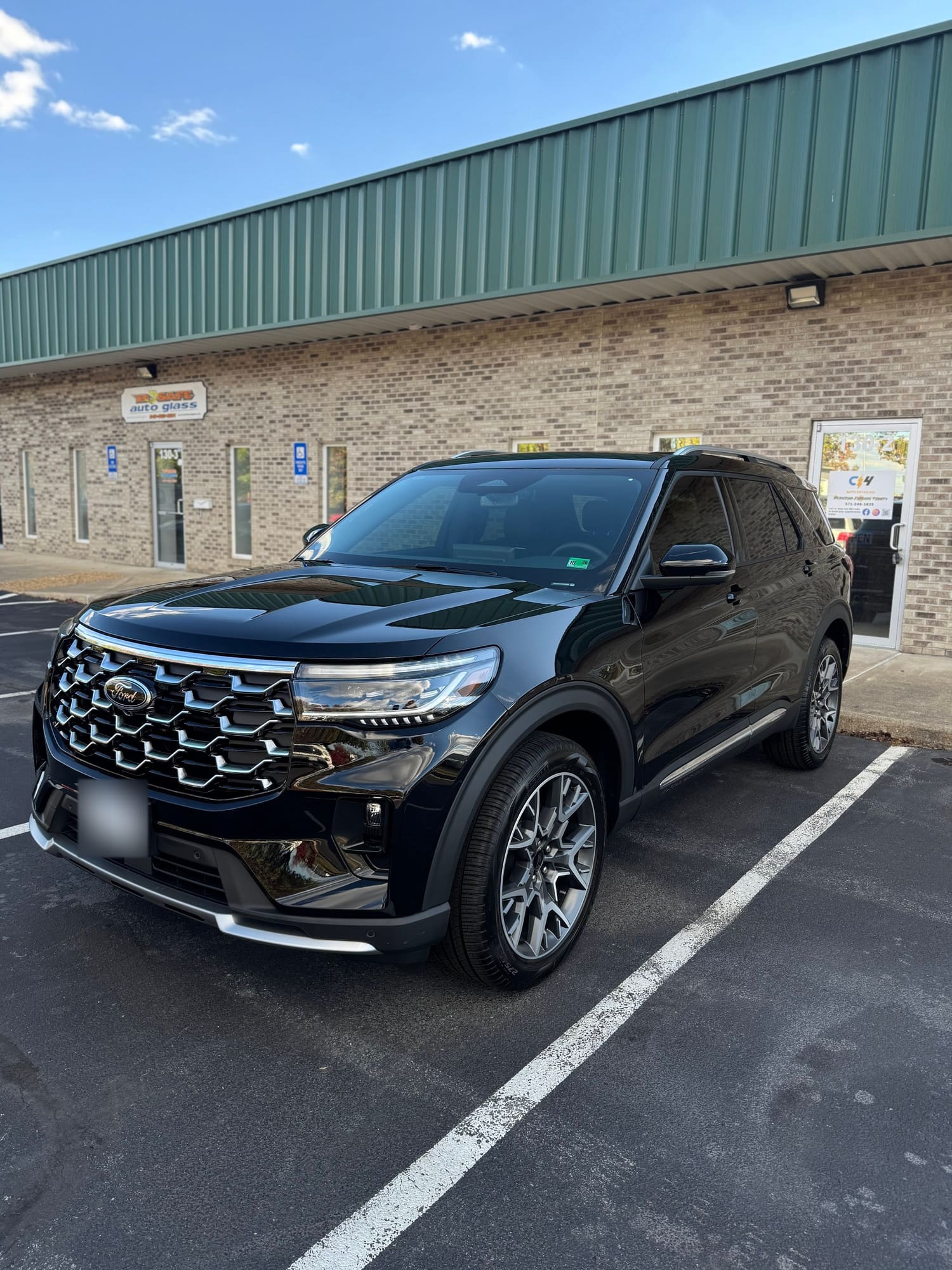 A black Ford SUV parked in a parking lot in front of a brick building with a green metal roof. The vehicle has a Virginia license plate and modern headlights.
