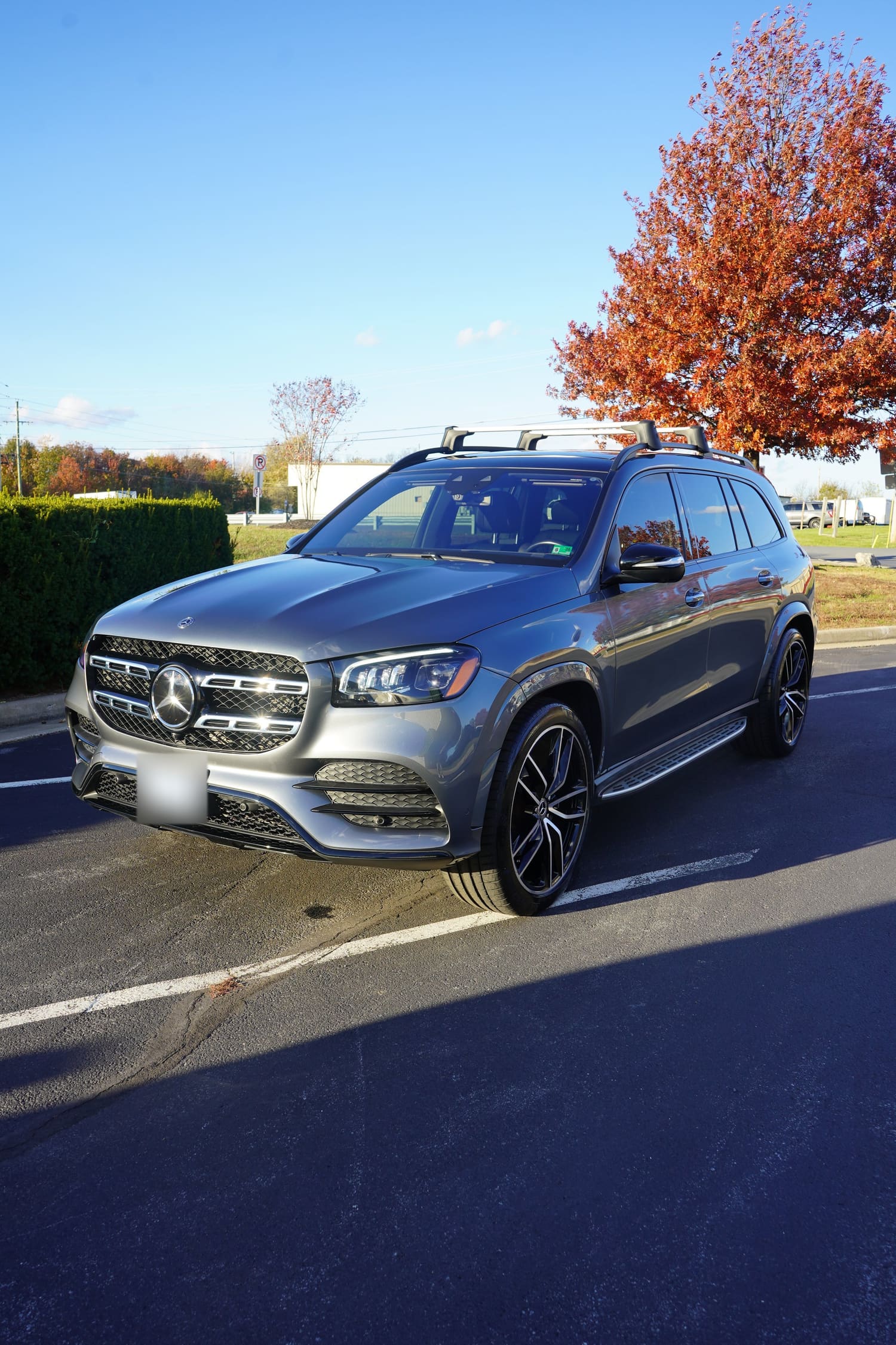 A gray Mercedes-Benz SUV parked in a lot during autumn with a tree with orange leaves in the background.