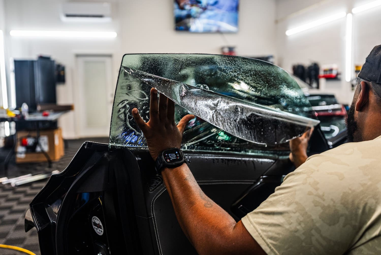 Technician fitting window tint film to a car door window