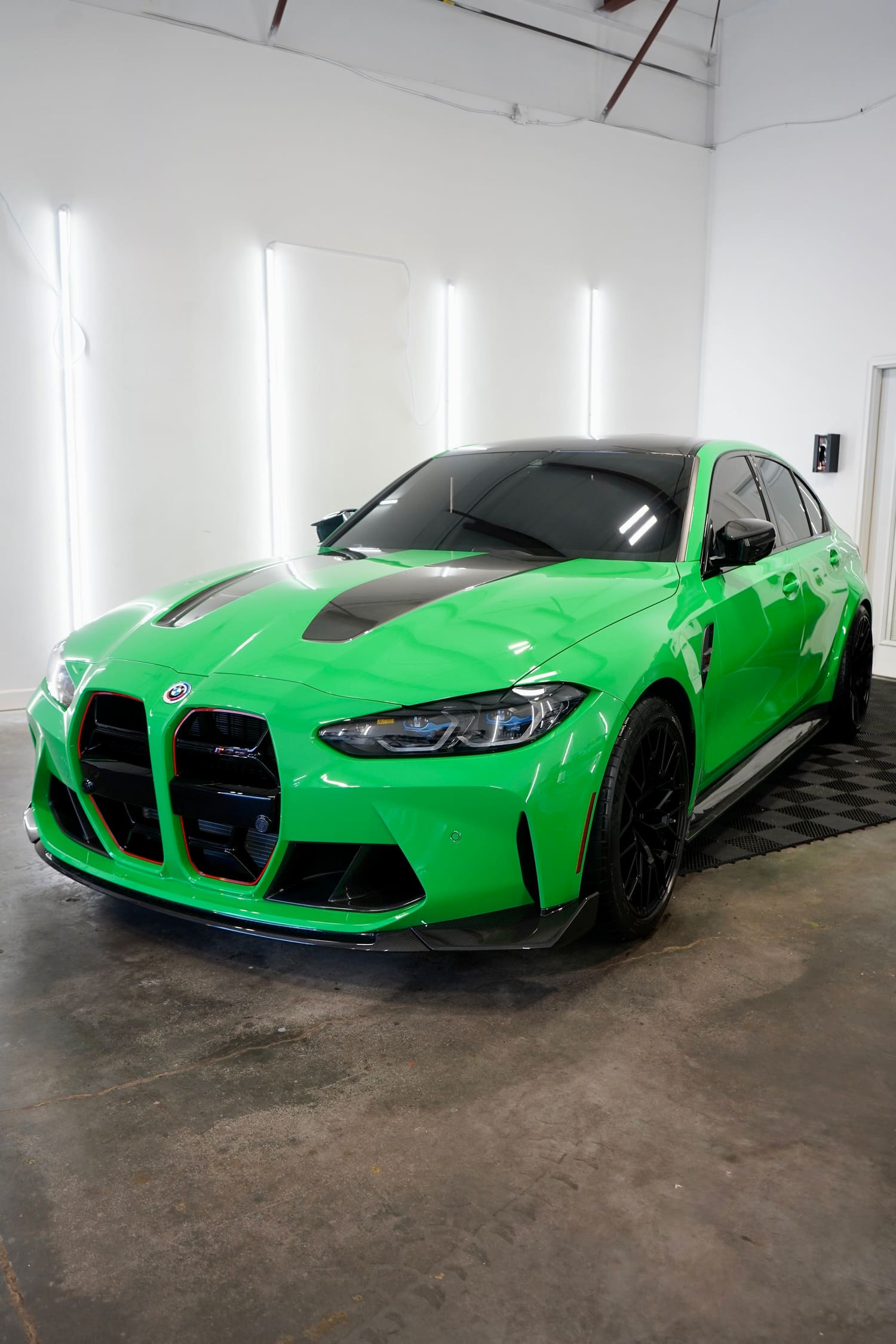 A bright green BMW sports car with black accents and a black roof in a showroom or garage with white walls and fluorescent lighting.