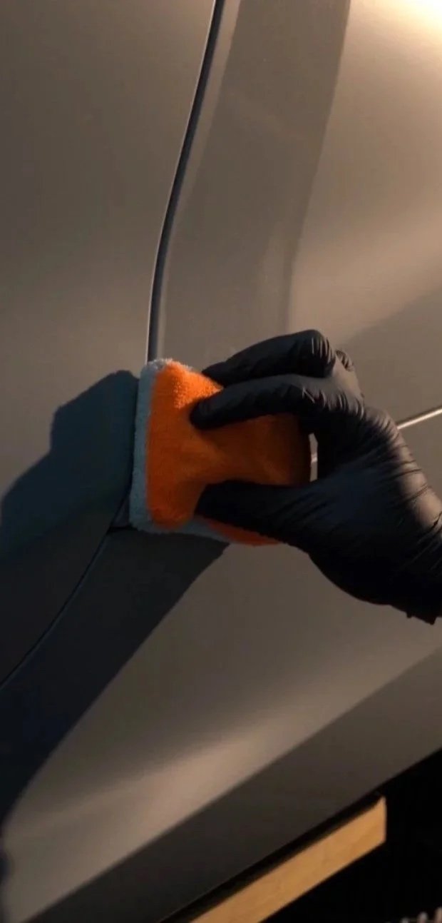 Person cleaning or polishing a gray cabinet door with a stitched cleaning cloth, wearing a black glove.