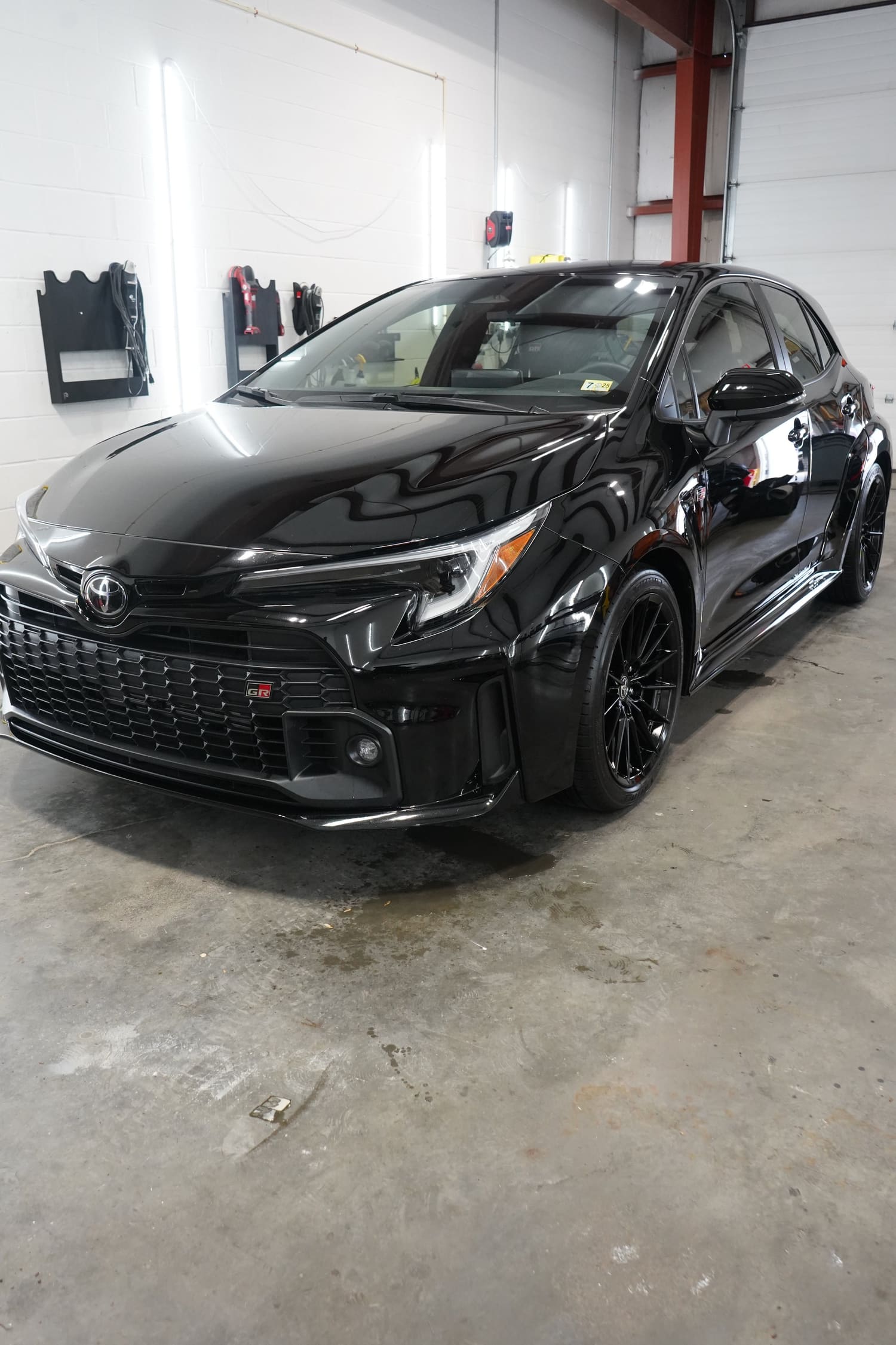 A black Toyota GR car parked inside a garage with white walls and concrete floor.