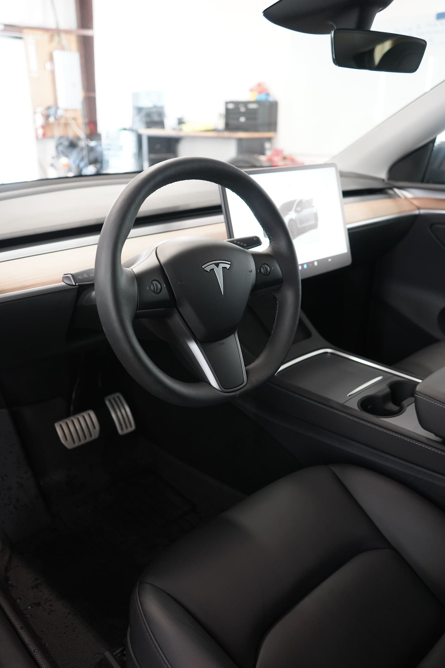 Interior of a Tesla vehicle, featuring a steering wheel with Tesla logo, digital display screen, and black leather seats.