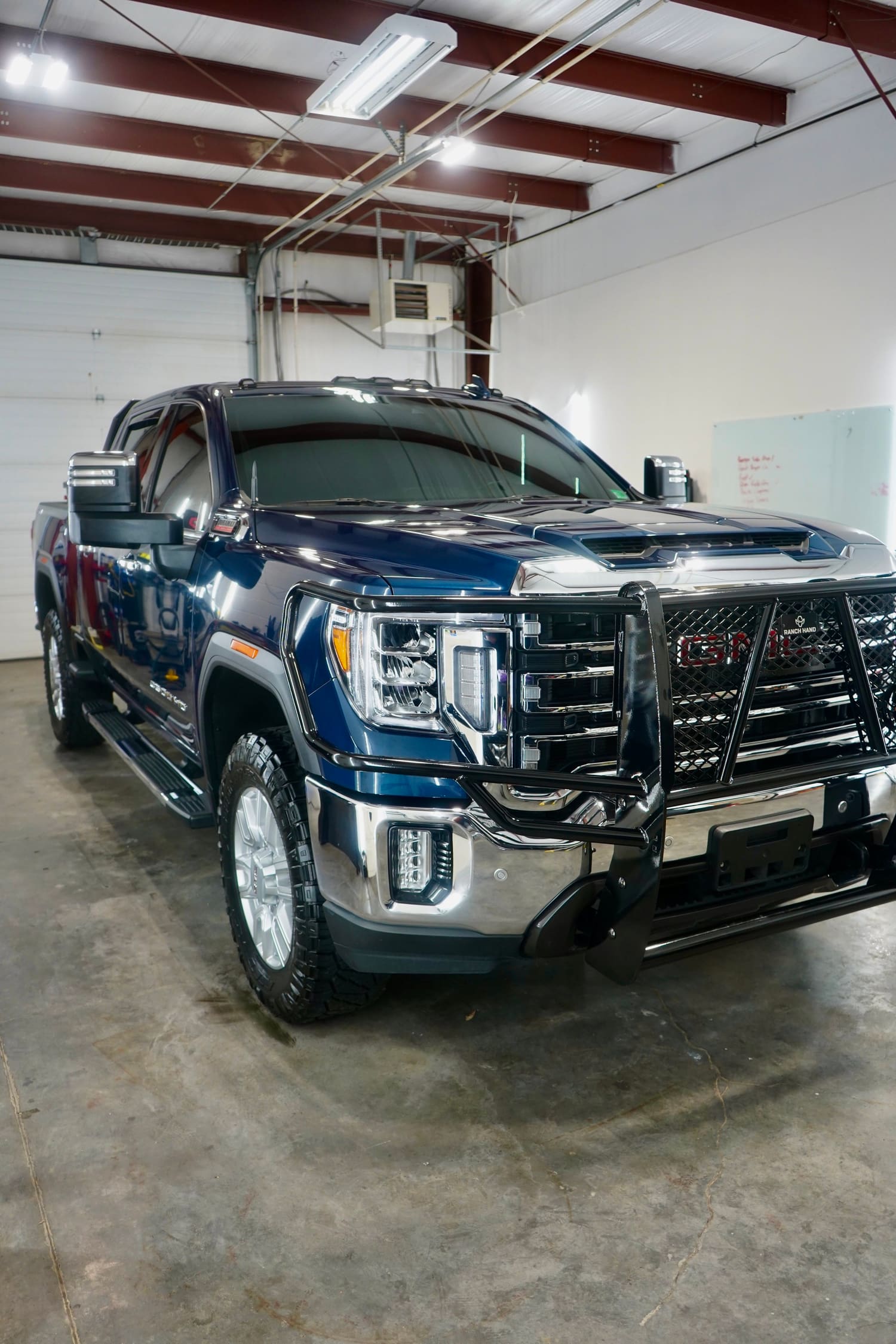 A blue GMC Sierra pickup truck with a black front grille guard inside a garage.