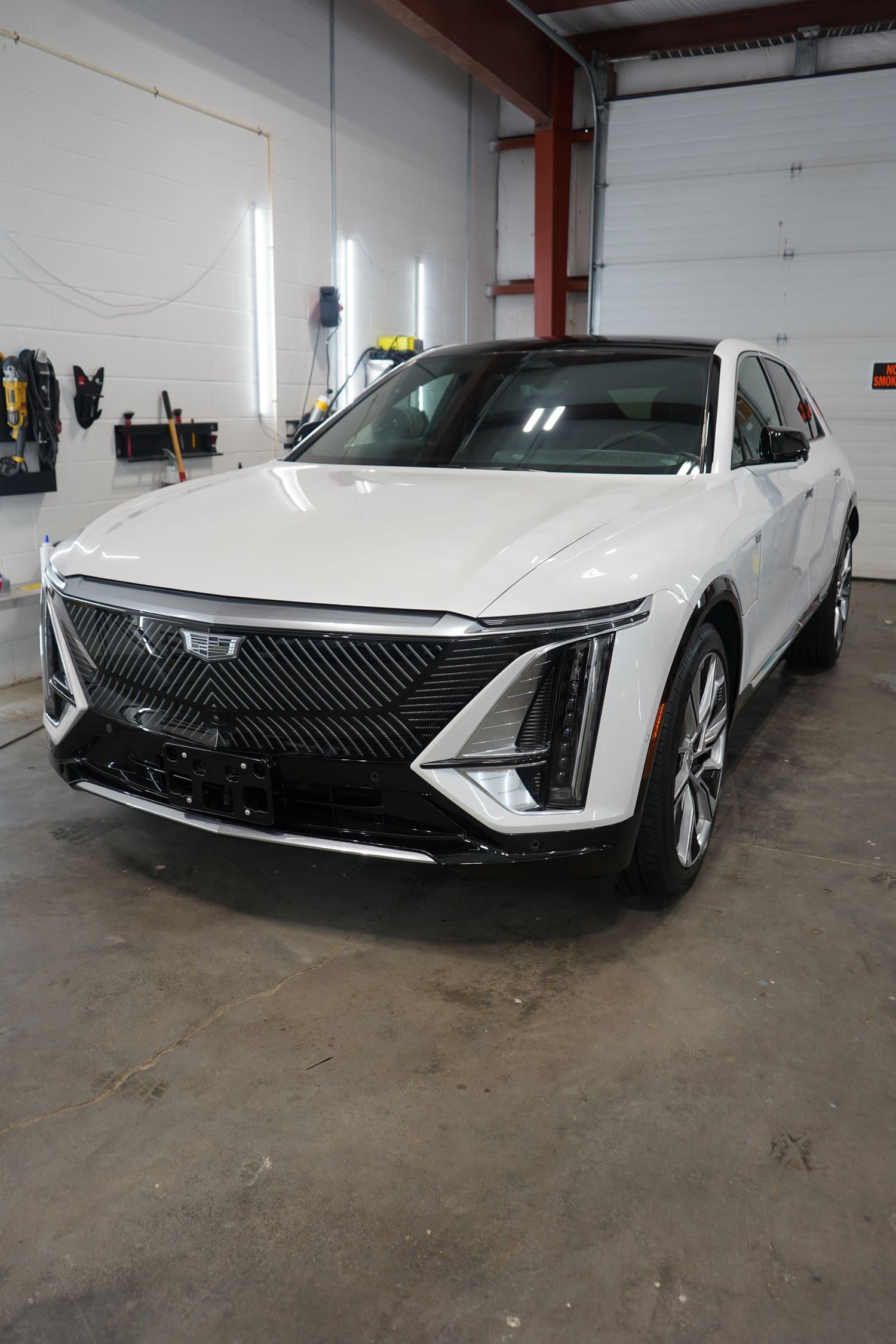 A white Cadillac SUV parked inside a garage with tools on the wall behind it.