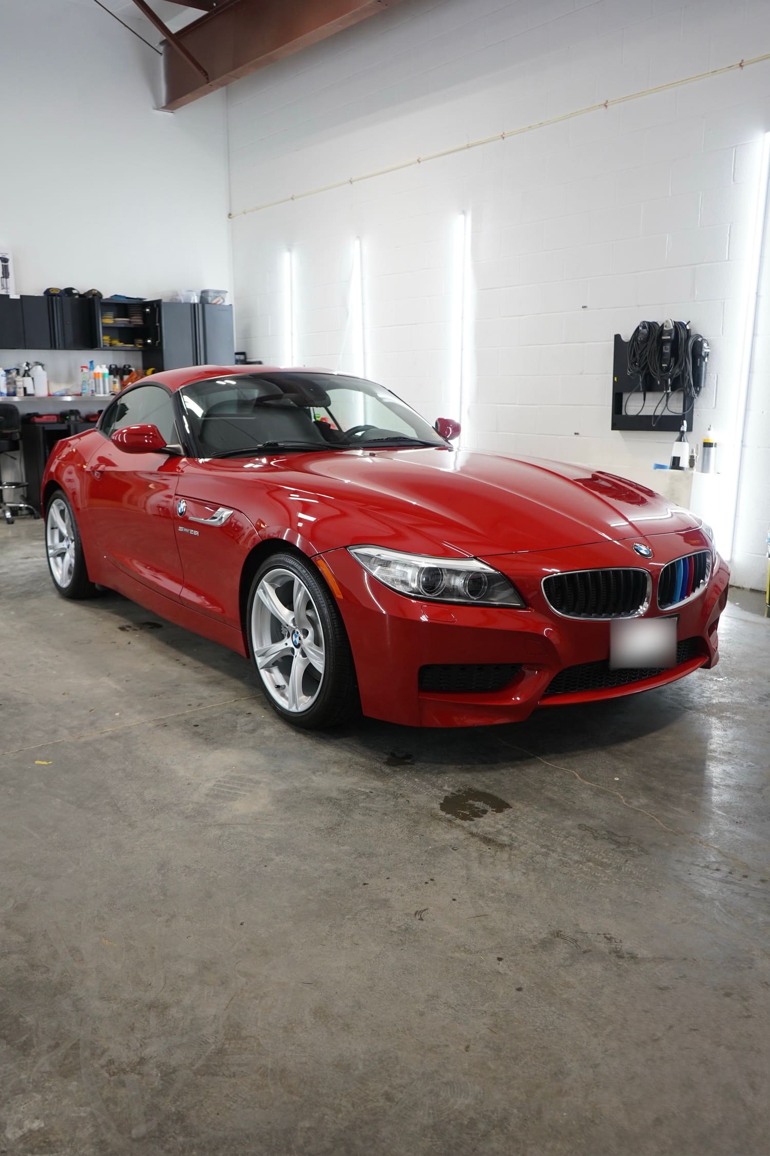 Red BMW Z4 convertible car parked inside a garage with white walls and concrete floor.